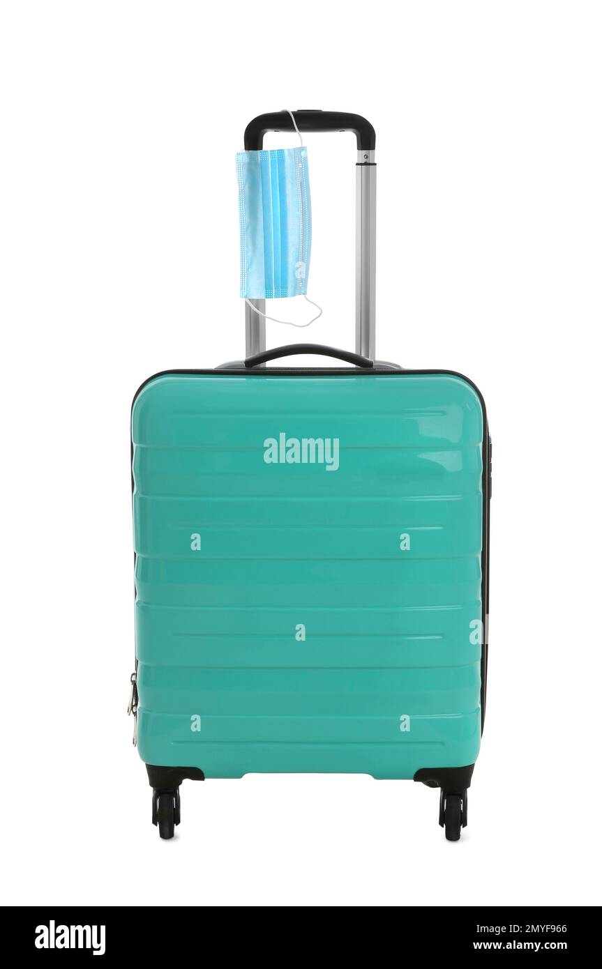 Elegante valigia turchese e maschera protettiva su sfondo bianco. Viaggiare durante la pandemia di coronavirus Foto Stock