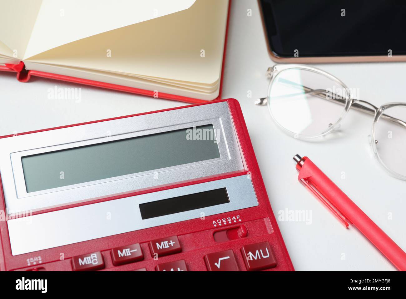 Calcolatrice, occhiali, smartphone e cancelleria su tavolo bianco, primo piano. Contabilità fiscale Foto Stock
