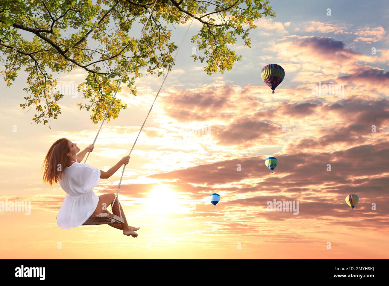 Il mondo dei sogni. Giovane donna che oscilla, palloncini ad aria calda in cielo tramonto sullo sfondo Foto Stock