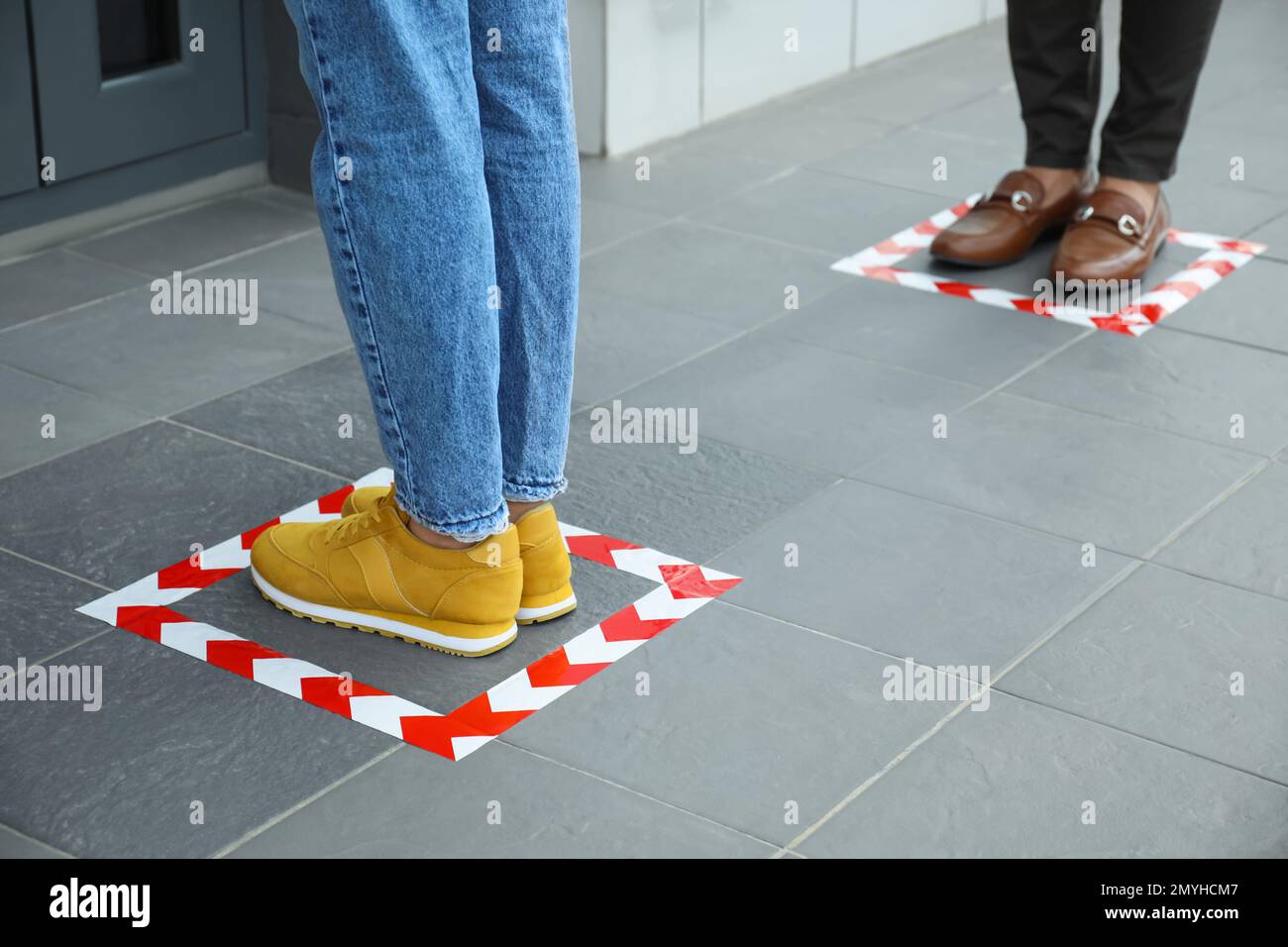 Persone in piedi su marcature a pavimento con nastro per distanza sociale, primo piano. Pandemia di coronavirus Foto Stock