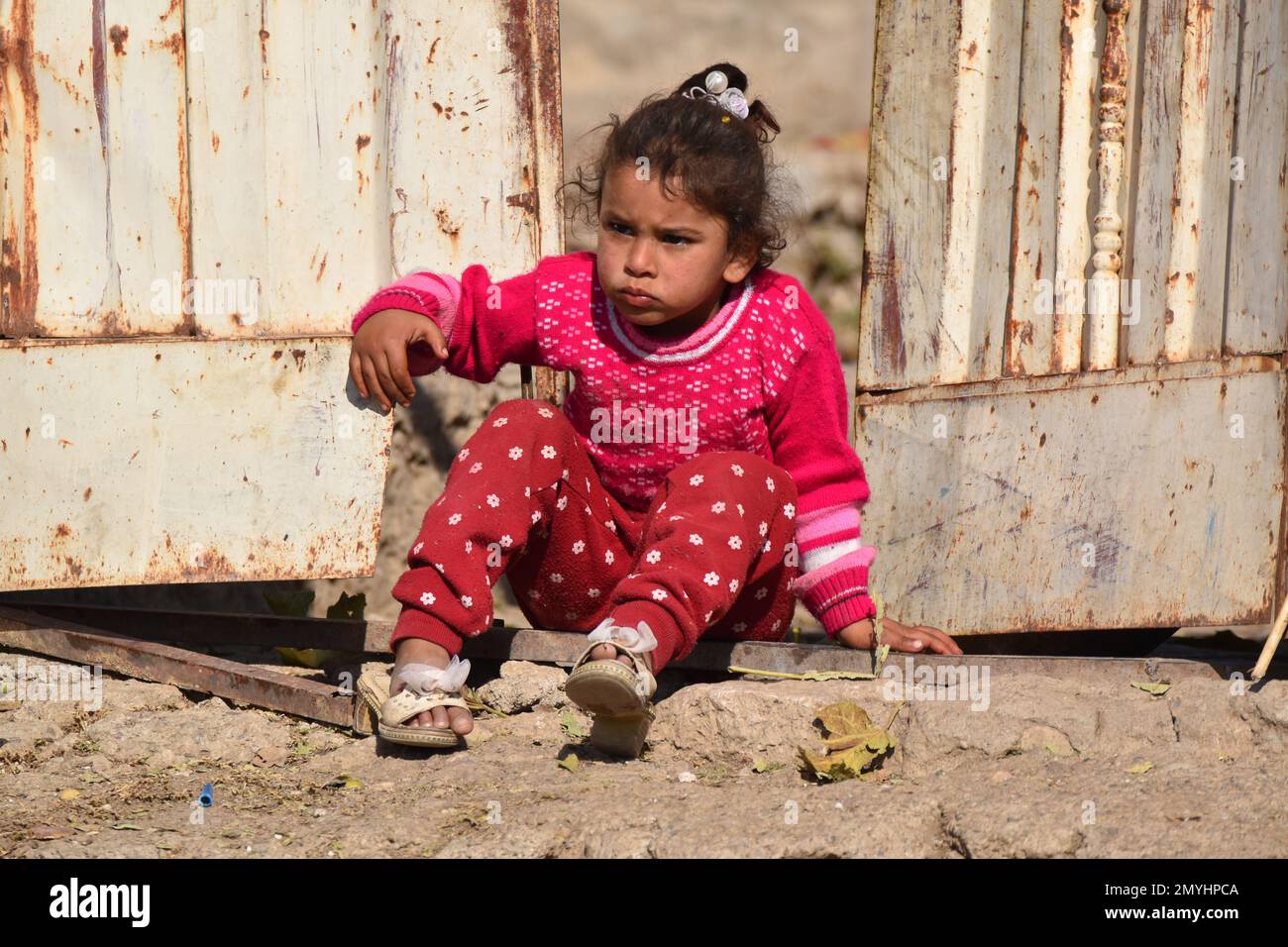 Una bambina con un'espressione seria guarda come gli sconosciuti camminano oltre la sua casa. Foto Stock