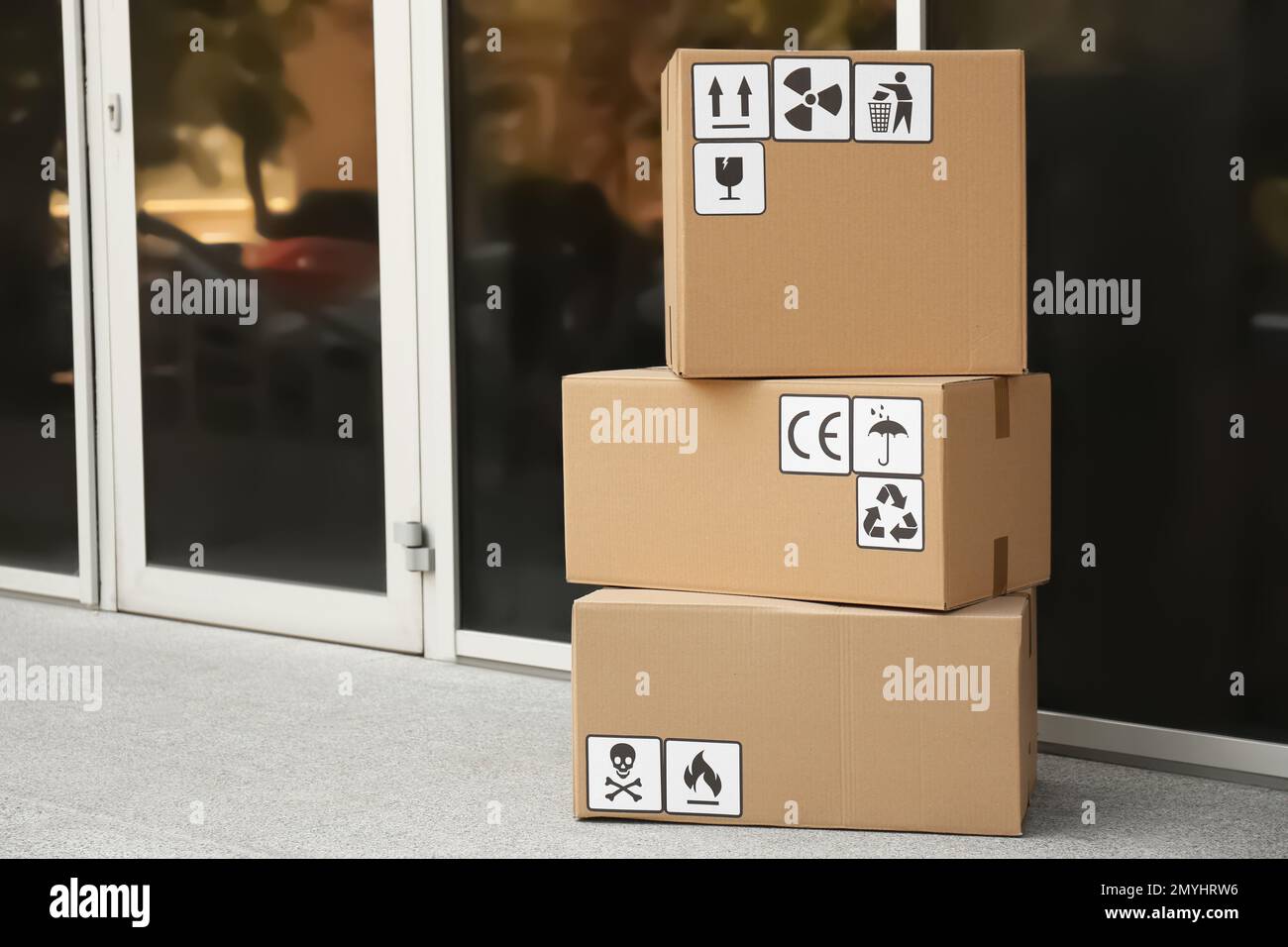 Scatole di cartone con diversi simboli di imballaggio sul pavimento vicino all'ingresso, spazio per il testo. Consegna pacchi Foto Stock