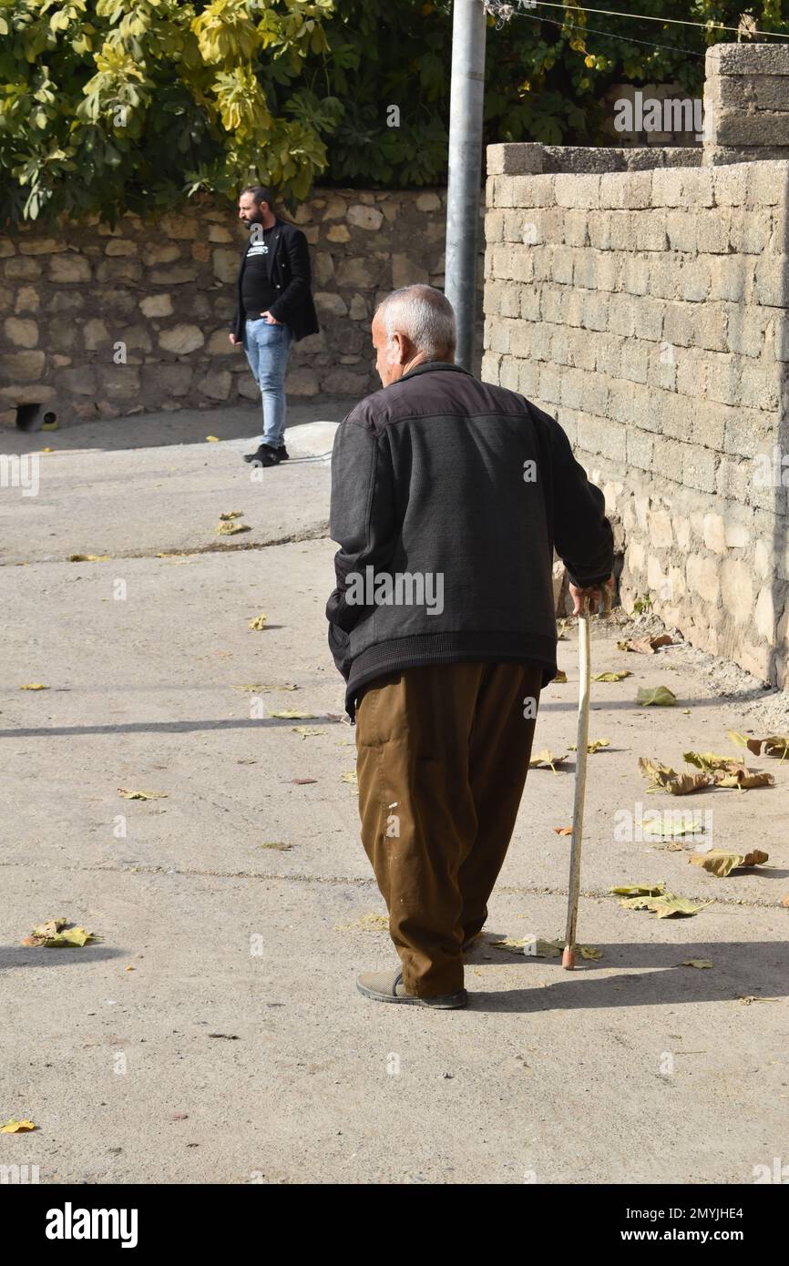 Un uomo anziano cammina con una canna lungo la strada del suo villaggio nel nord dell'Iraq Foto Stock