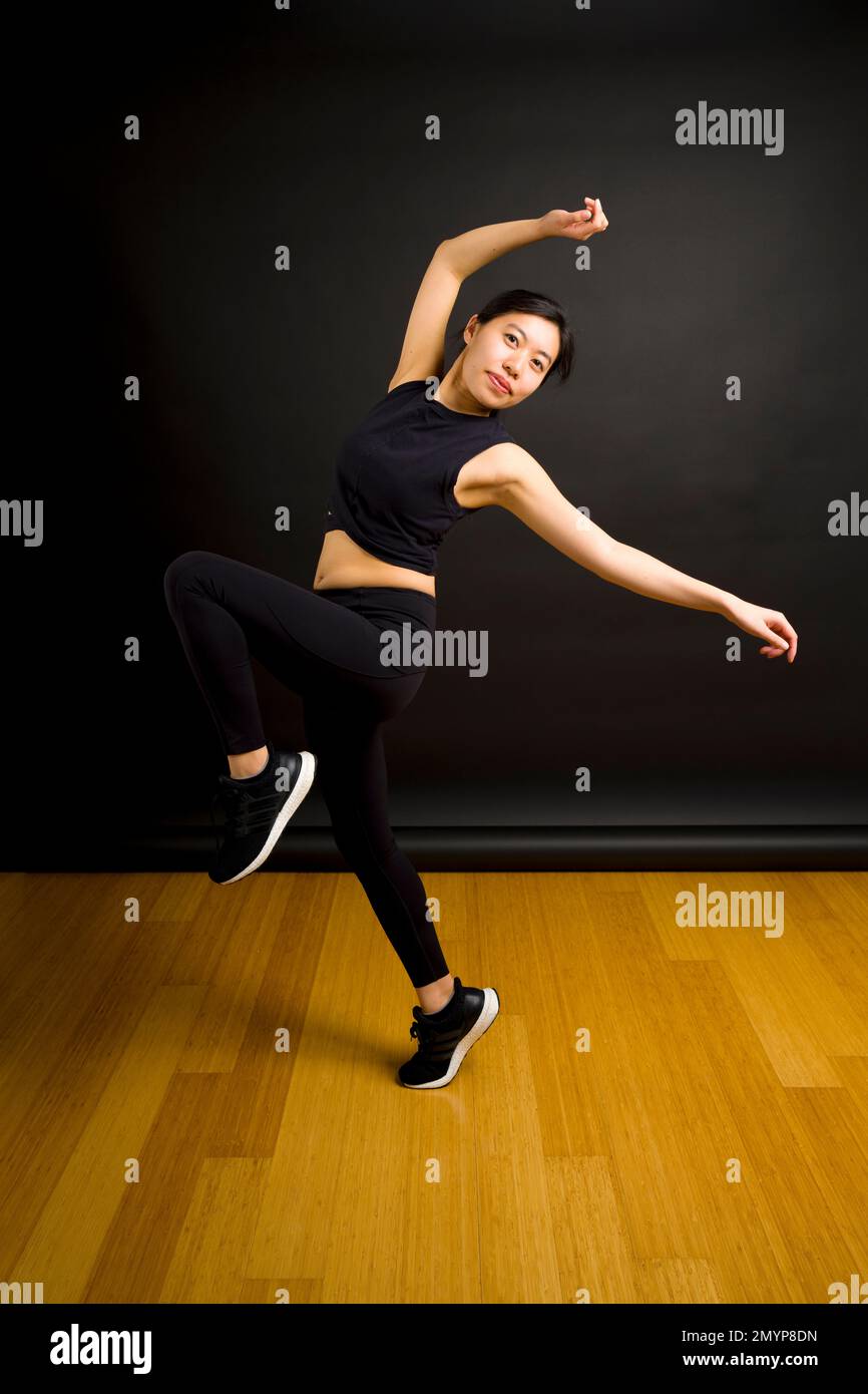Giovane ballerina asiatica che lancia le armi in aria di fronte allo sfondo nero Foto Stock