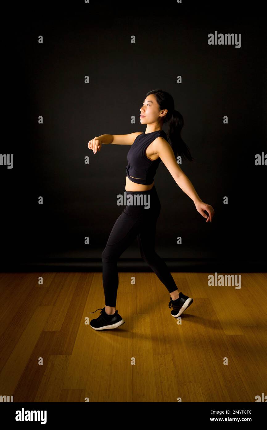 Giovane ballerina asiatica che lancia le armi in aria di fronte allo sfondo nero Foto Stock