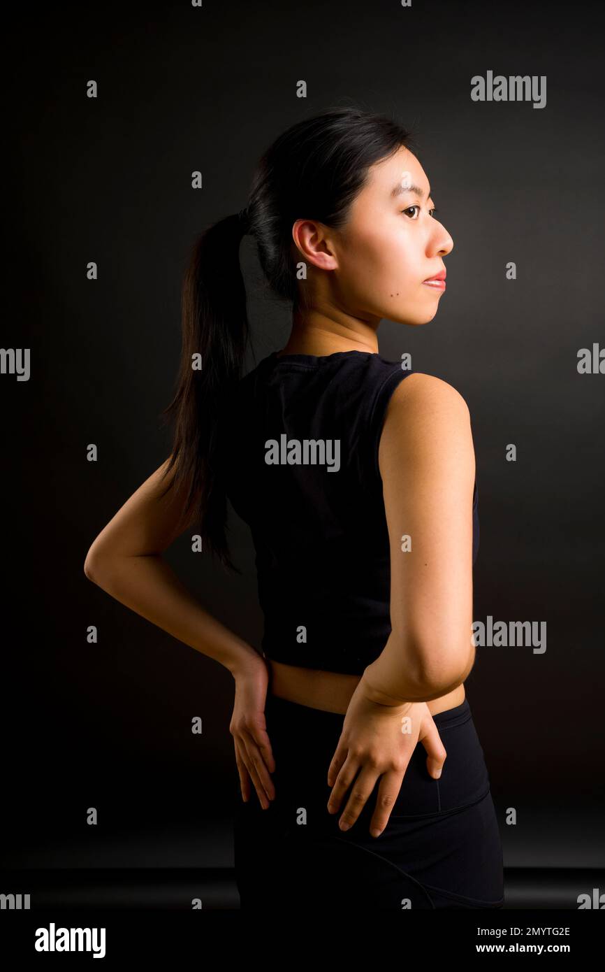 1/2 Body Back View of Young Asian Woman with Ponytail in Profile with Hands on HIPS Foto Stock