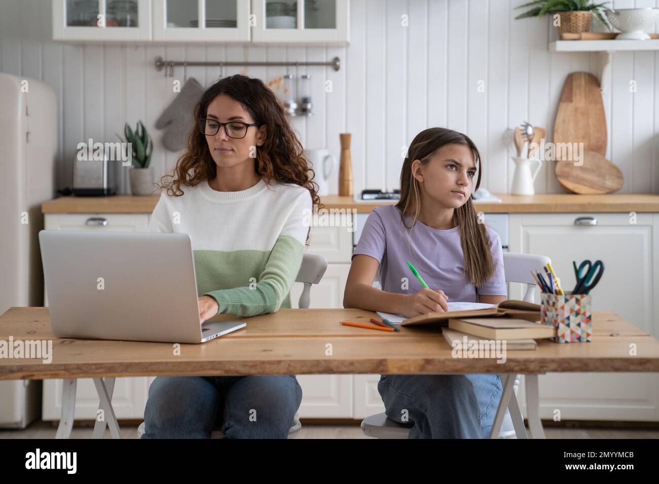 Donna di affari concentrata di successo mamma che fa lavoro al notebook si siede al tavolo da cucina vicino con la figlia Foto Stock