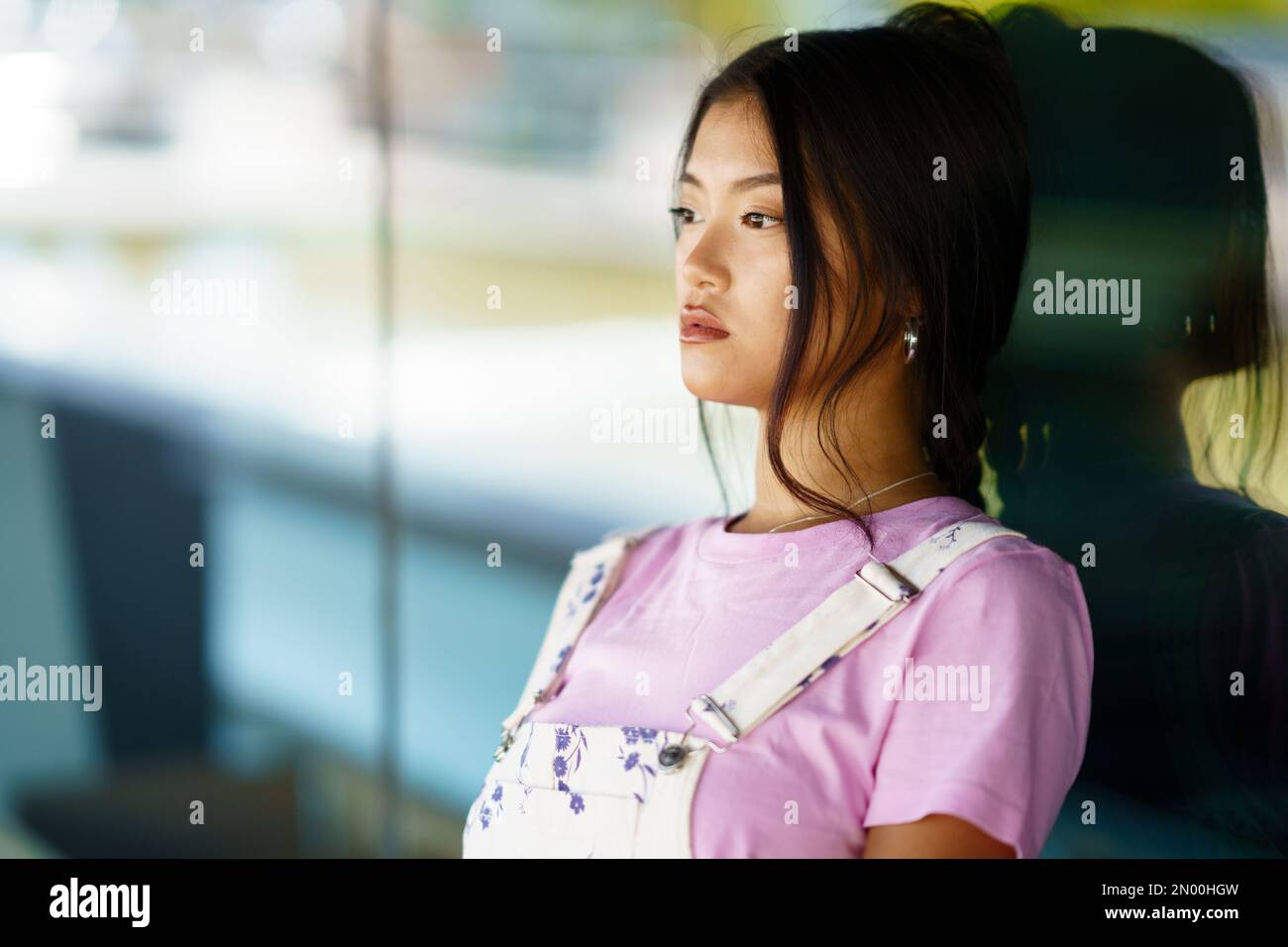 Donna asiatica appoggiata su una parete di vetro Foto Stock