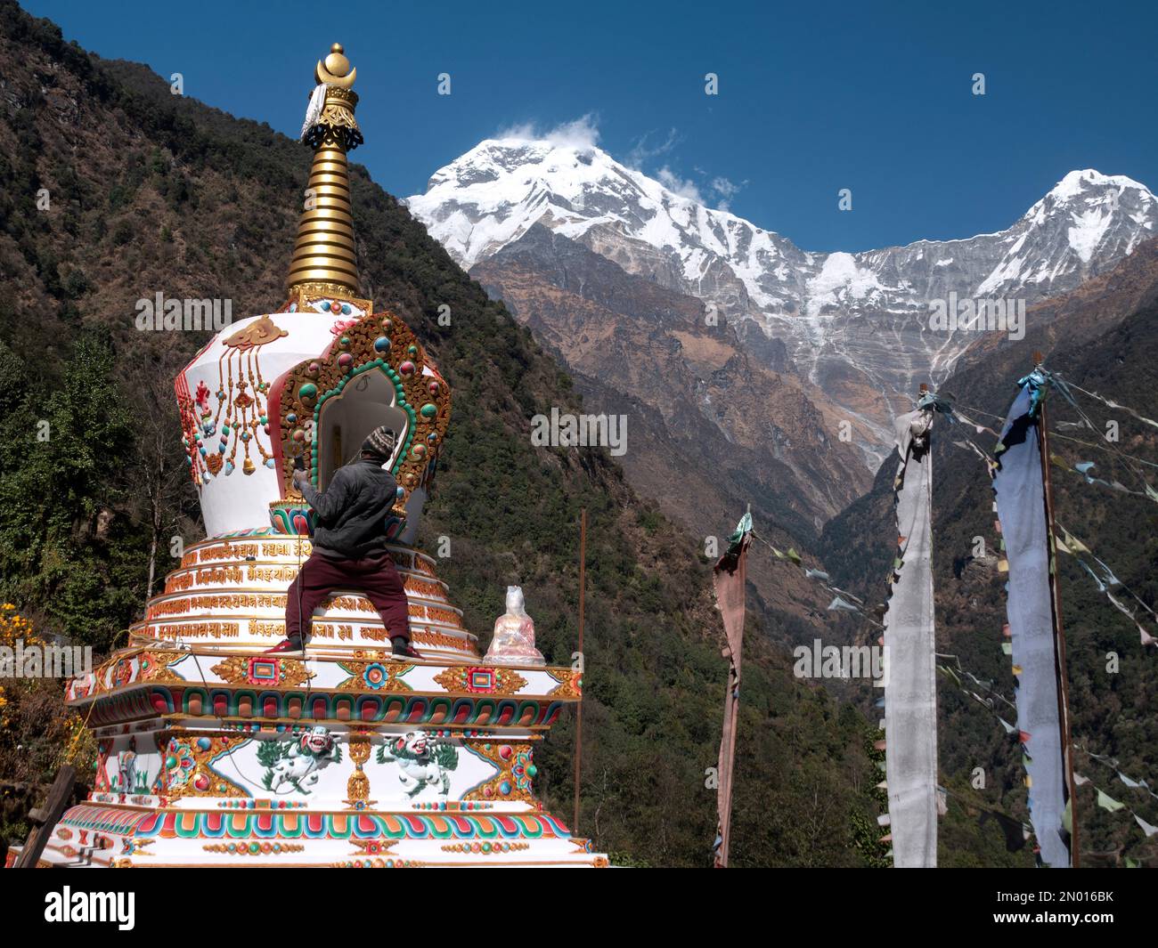 Chhomrong, Nepal. Uomo gli ultimi dettagli del nuovo villaggio buddista stupa. Bandiere e Annapurna Sud sullo sfondo. Foto Stock
