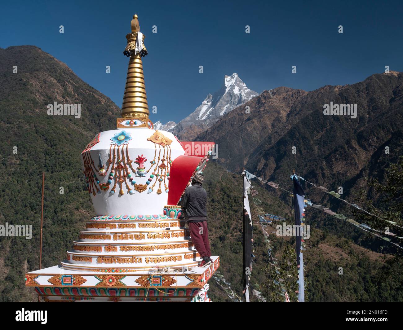 Chhomrong, Nepal. Uomo che finisce gli ultimi dettagli del nuovo villaggio stupa. Mt Fishtail Machapuchare sullo sfondo. Foto Stock
