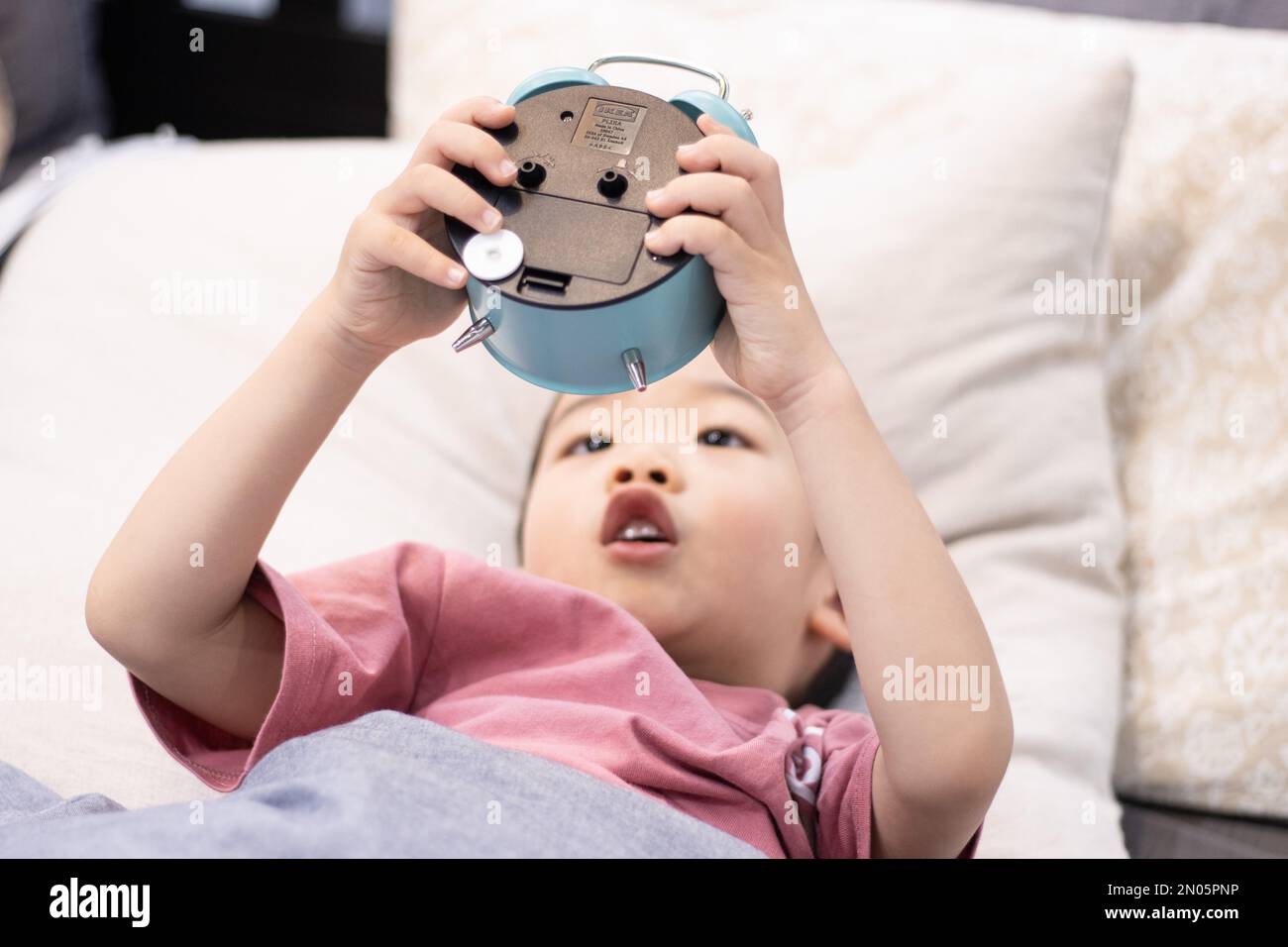 Un ragazzino sdraiato sul letto per vedere la sveglia Foto Stock