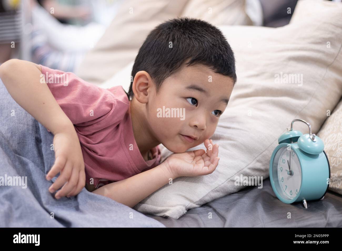 Un ragazzino sdraiato sul letto per vedere la sveglia Foto Stock