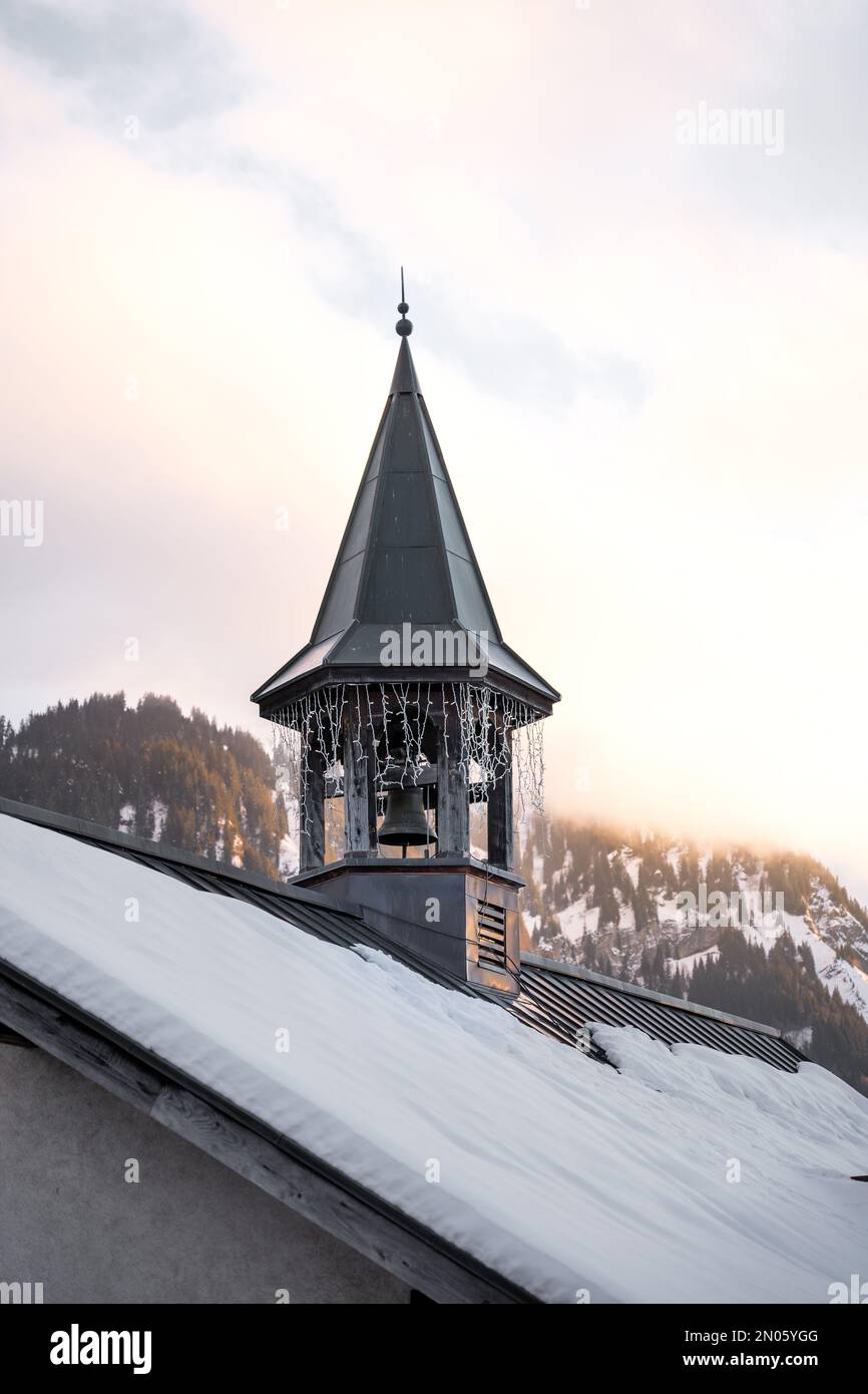 vista su un campanile decorato con una ghirlanda luminosa di un tetto con uno sfondo di montagna, sotto la calda luce d'oro d'inverno Foto Stock