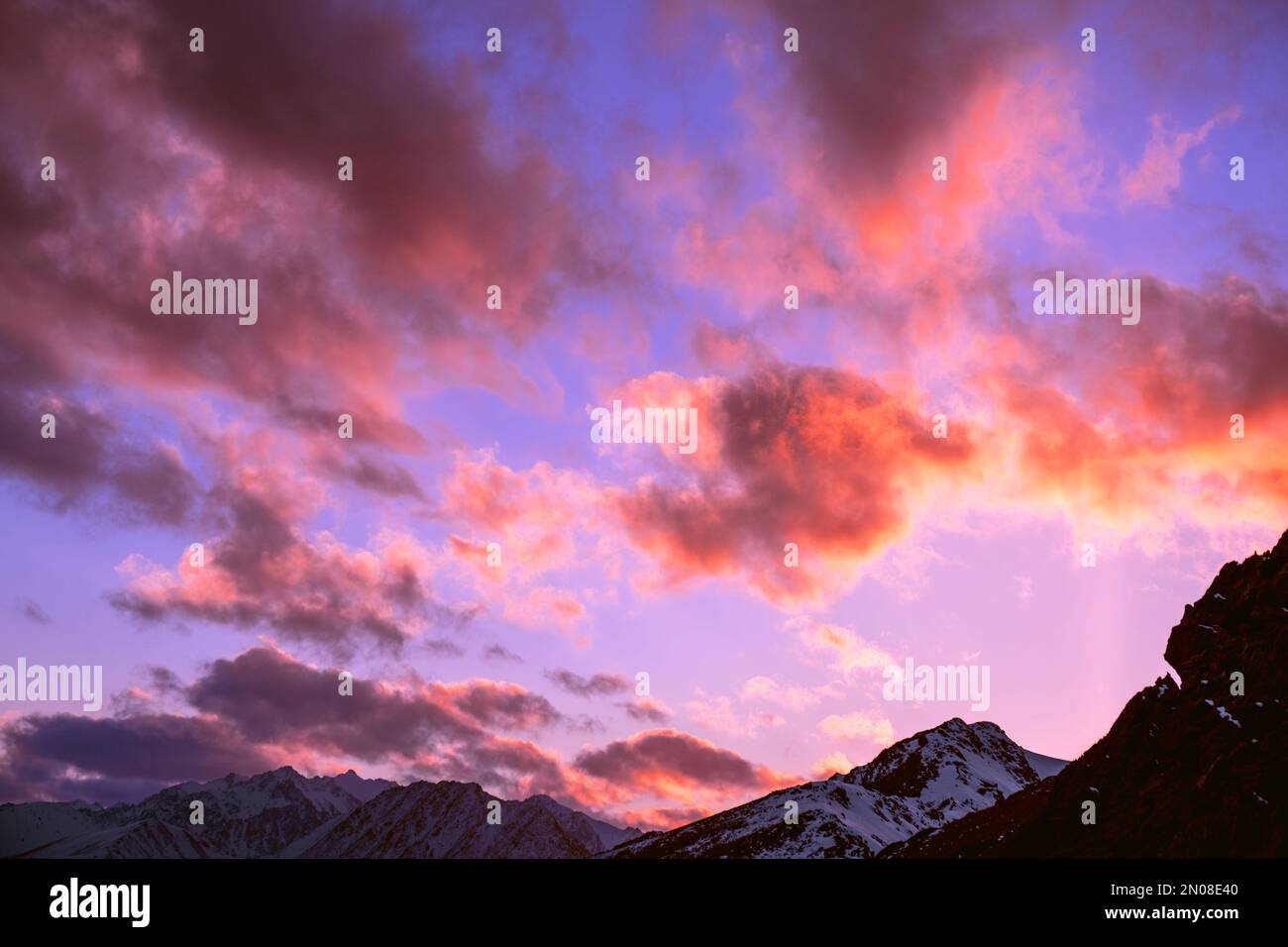 Nuvole bizzaramente interessanti al tramonto sulle cime innevate delle montagne Foto Stock