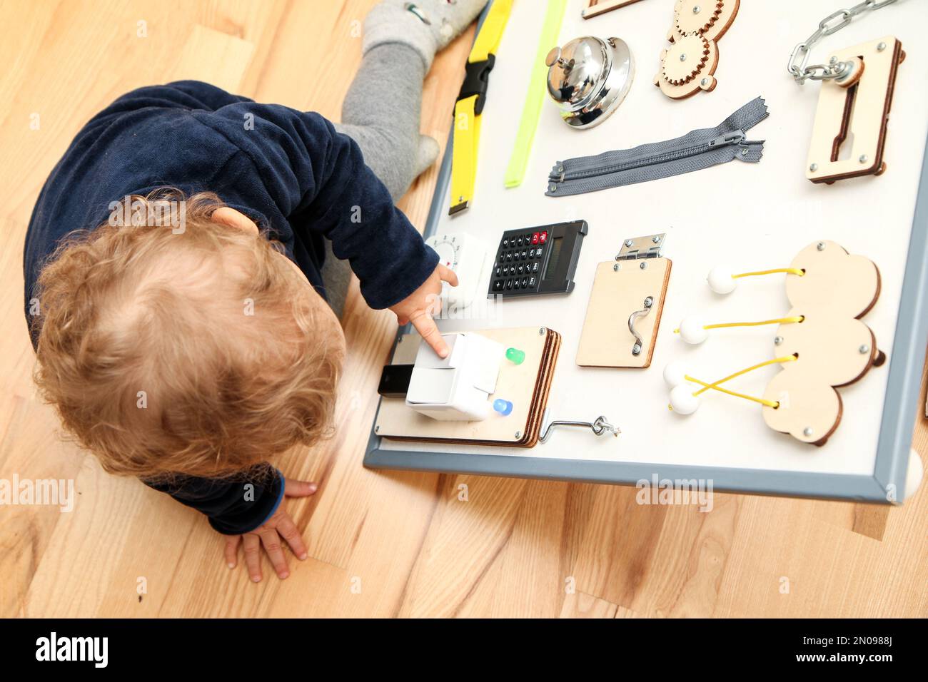 Il bambino piccolo gioca con la bacheca delle attività per ottenere una nuova esperienza, mettere in pratica le sue competenze e ottenere un miglioramento durante la sua crescita. Foto Stock