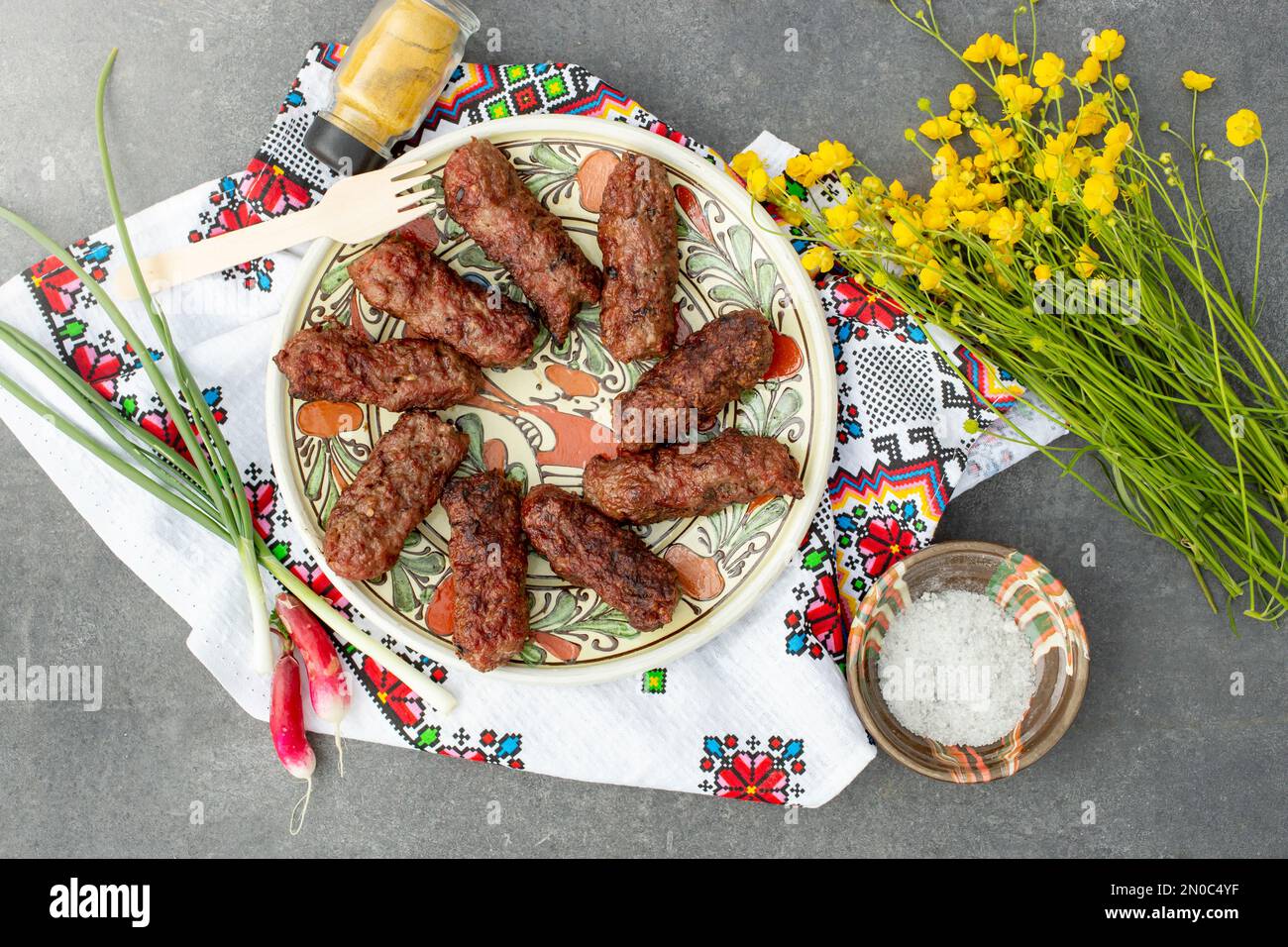 rotoli di carne tradizionali, detti “mititei” su un piatto di ceramica, con un bouquet di fiori di tazzina Foto Stock