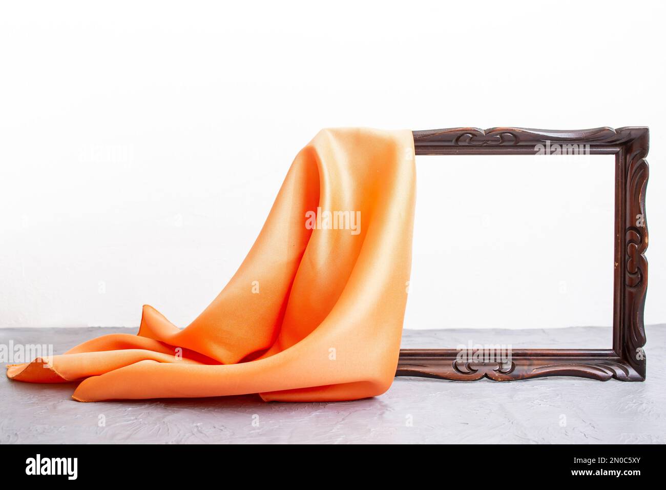 Tela di raso arancione che svela una cornice di legno marrone, su piano tavolo in cemento e sfondo bianco, mockup per la presentazione Foto Stock