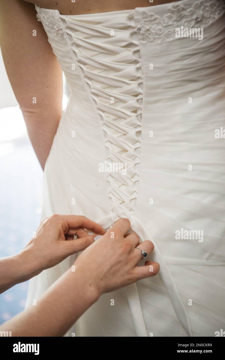 Un colpo verticale di una donna che fa un nodo d'arco sulla parte posteriore del vestito di nozze della sposa. Foto Stock