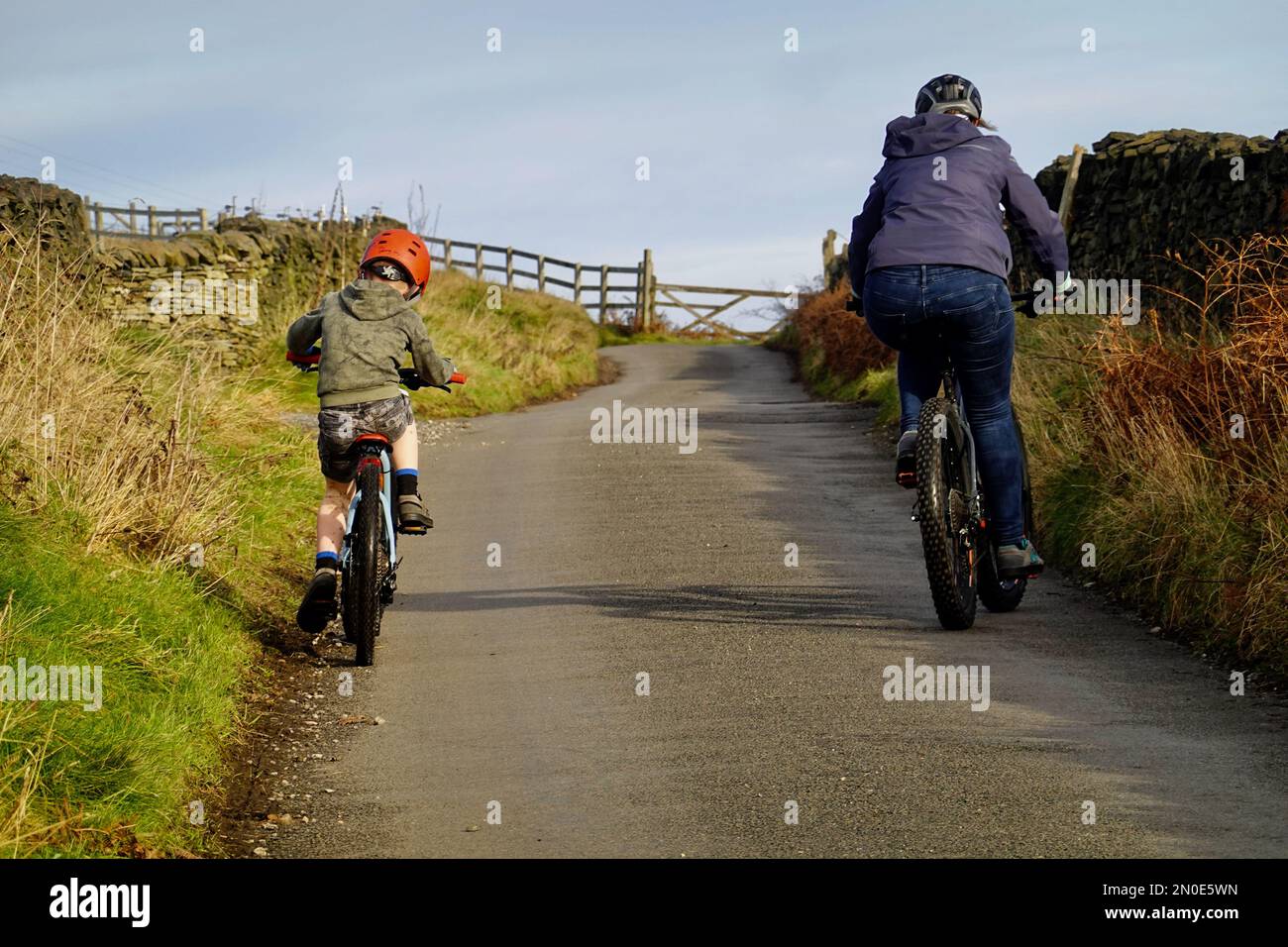 Una donna e un bambino pedalano su una ripida collina in Thornsett, Birch vale, Derbyshire Foto Stock