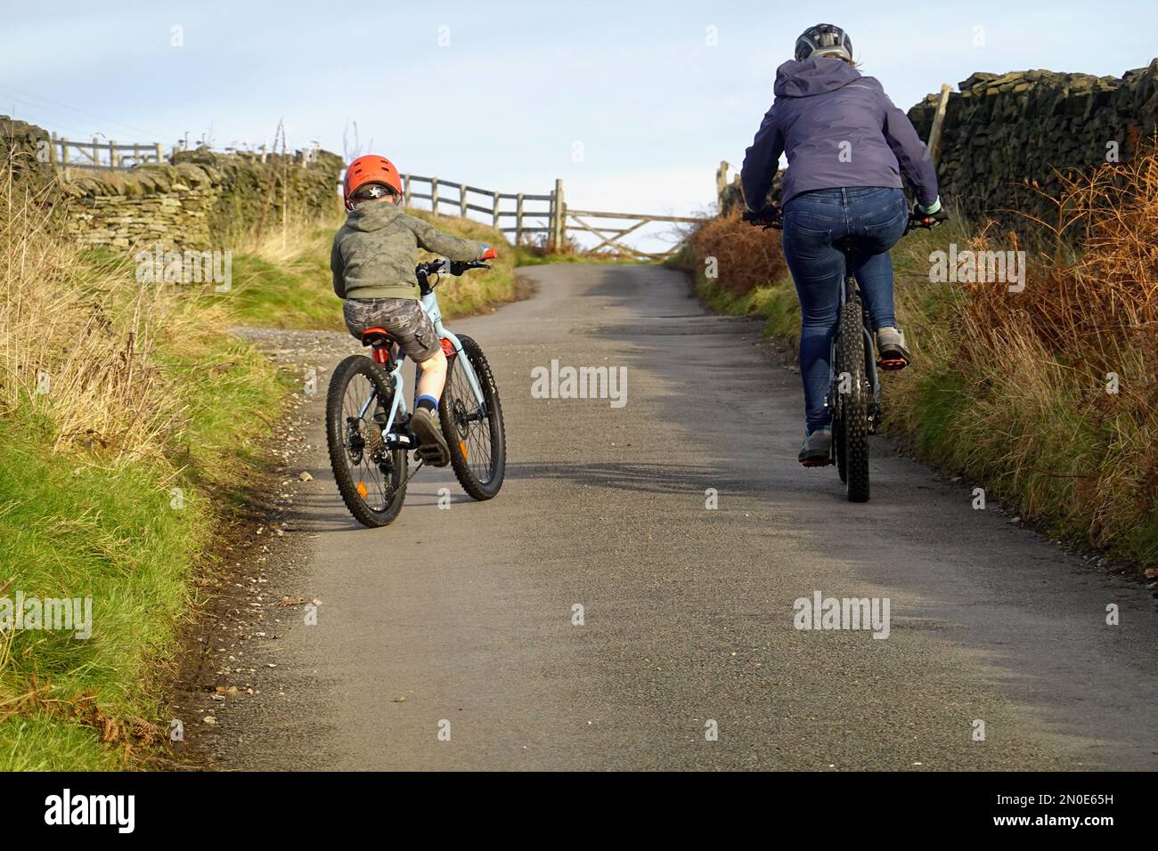 Una donna e un bambino pedalano su una ripida collina in Thornsett, Birch vale, Derbyshire Foto Stock