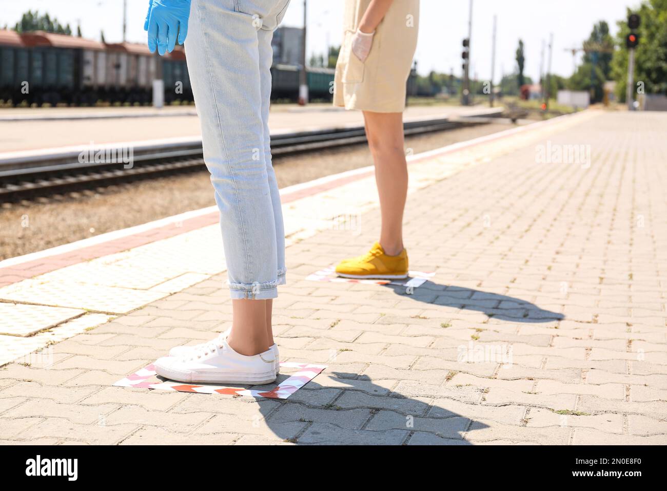 Persone in piedi su marcature a pavimento con nastro per la distanza sociale alla stazione ferroviaria, closeup. Pandemia di coronavirus Foto Stock