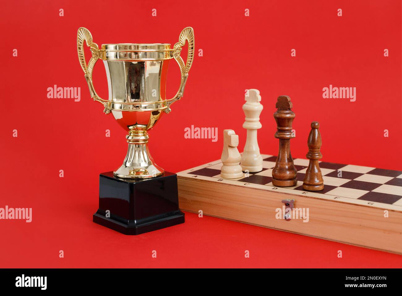 Coppa d'oro vincitrice e scacchiera con figure in legno ancora vita su sfondo rosso Foto Stock