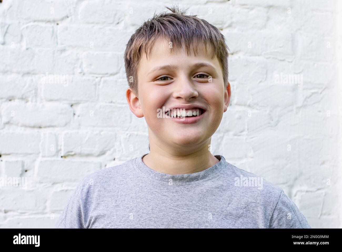il ragazzo sorride felicemente. Ritratto di un fantastico ragazzino amichevole. bell'adolescente vicino a un muro di mattoni bianchi Foto Stock