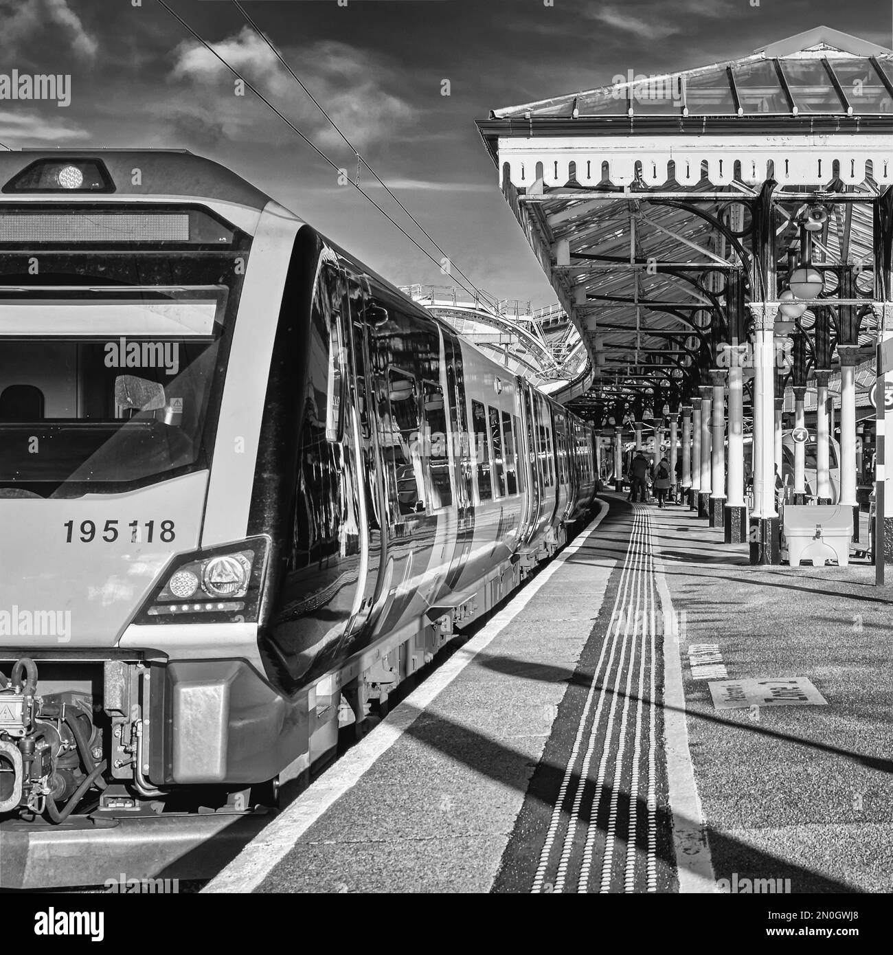 Vista di una stazione ferroviaria con rotaie che conducono verso un arco di ferro. Una piattaforma è coperta da una tettoia del 19th ° secolo e un treno è in primo piano Foto Stock