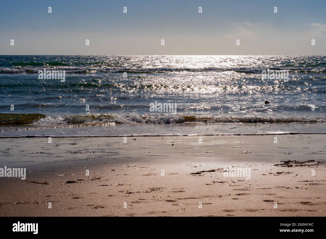 Le onde dell'oceano si infrangono contro una spiaggia sabbiosa in una giornata di sole Foto Stock