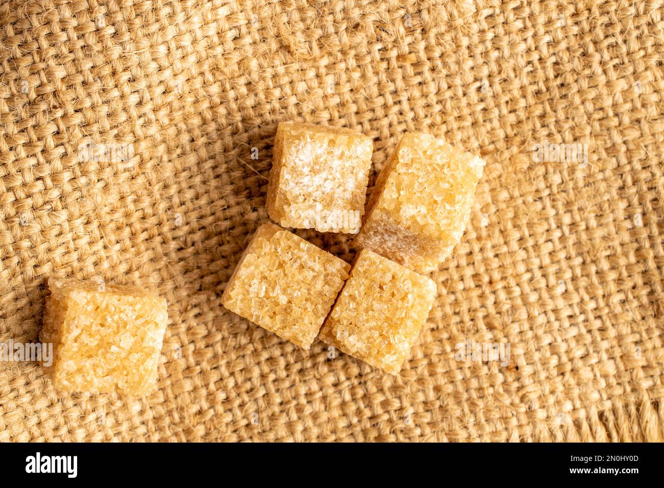 Diversi cubetti di zucchero di canna, primo piano, su un tessuto di iuta, vista dall'alto. Foto Stock