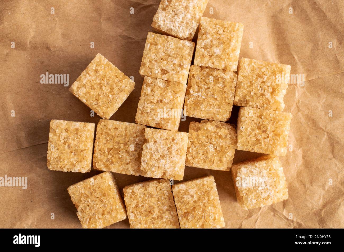 Diversi cubetti di zucchero di canna, primo piano, su carta marrone, vista dall'alto. Foto Stock