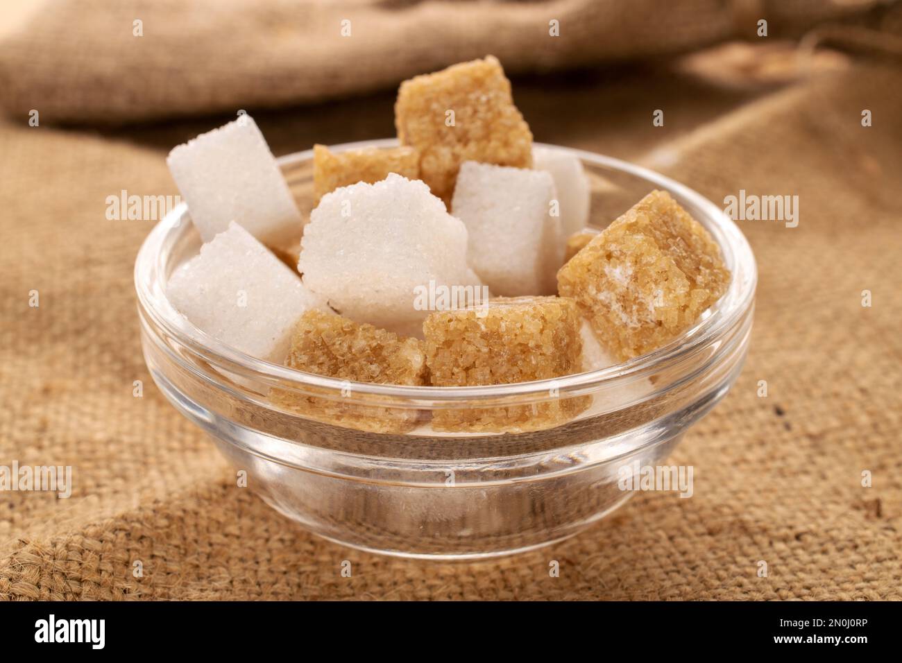 Diversi cubetti di zucchero di canna e bianco, da vicino, su un tessuto di iuta. Foto Stock