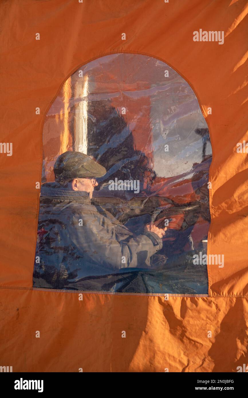 Uomo che naviga il telefono cellulare visto attraverso una finestra di plastica di una tenda bar in piazza del mercato di Helsinki Foto Stock