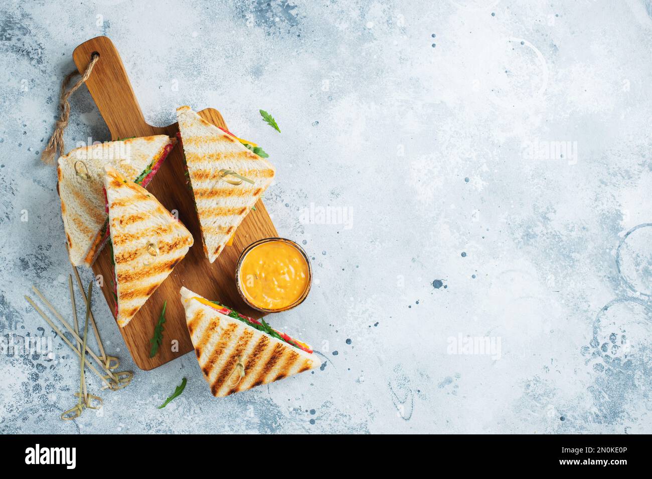 Quattro panini fatti in casa con salsiccia, formaggio e rucola su un fondo di cemento chiaro. Il concetto di un pasto veloce o uno spuntino al lavoro o a scuola. Foto Stock