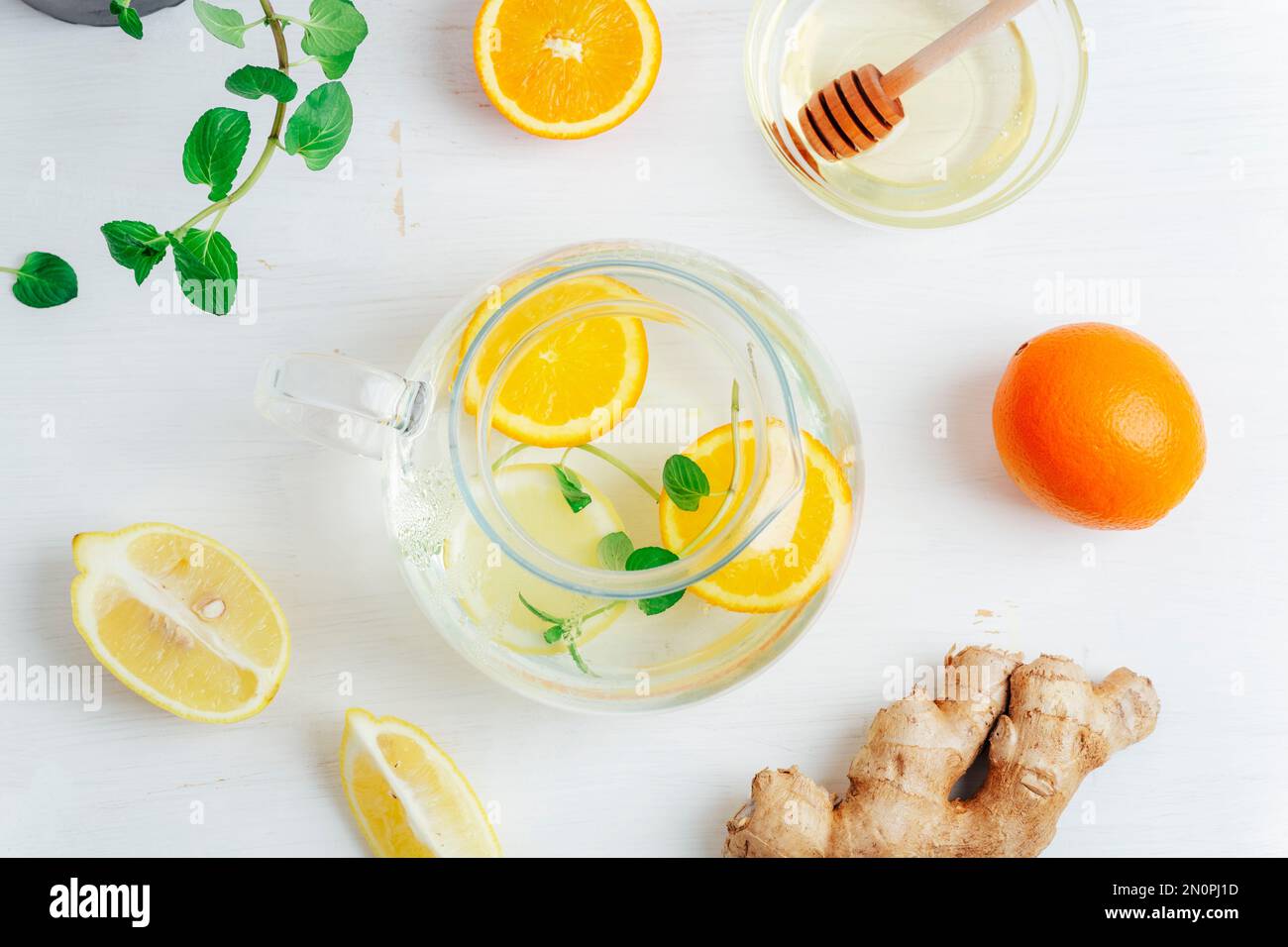 Teiera di vetro con tè all'arancia, al limone, allo zenzero e alla menta con ingredienti su un tavolo di legno bianco. Vista dall'alto, disposizione piatta. Foto Stock