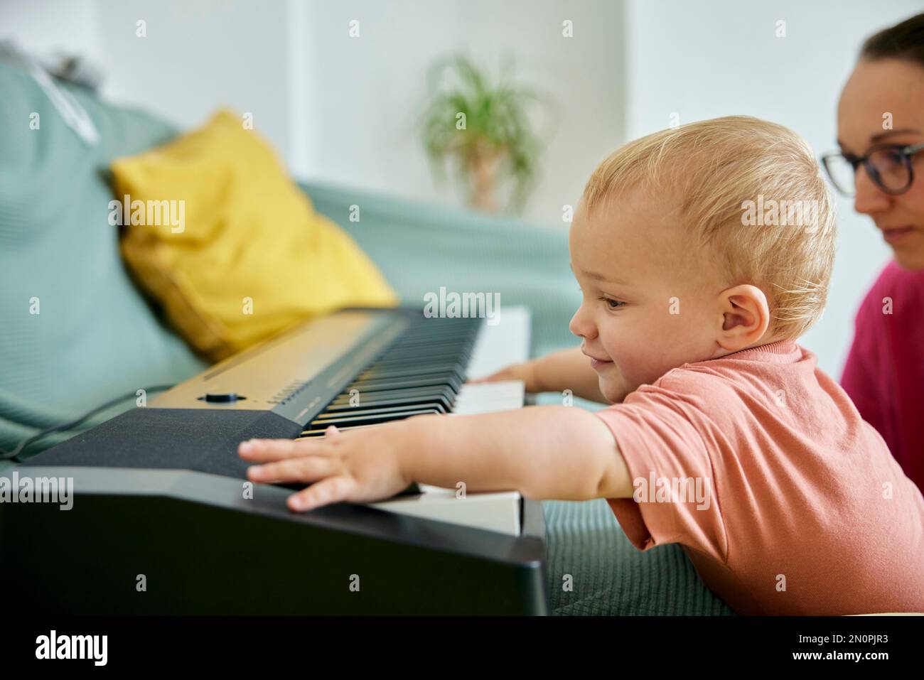 Il bambino gioca con la tastiera elettronica del pianoforte sul divano Foto Stock