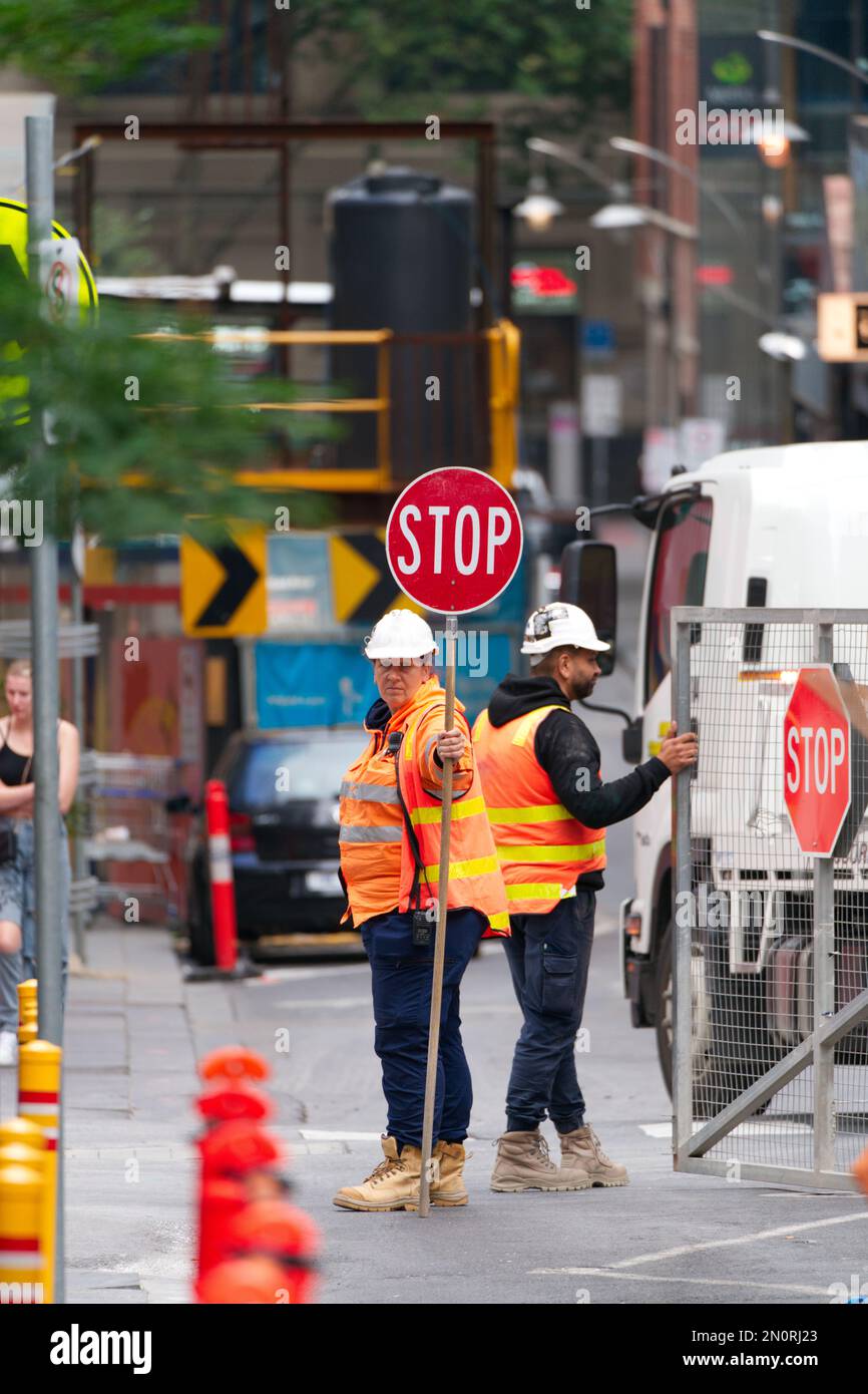Ufficiale di controllo del traffico donna in possesso di un segnale di stop rosso indossare dpi, cantiere Melbourne città Australia. Foto Stock