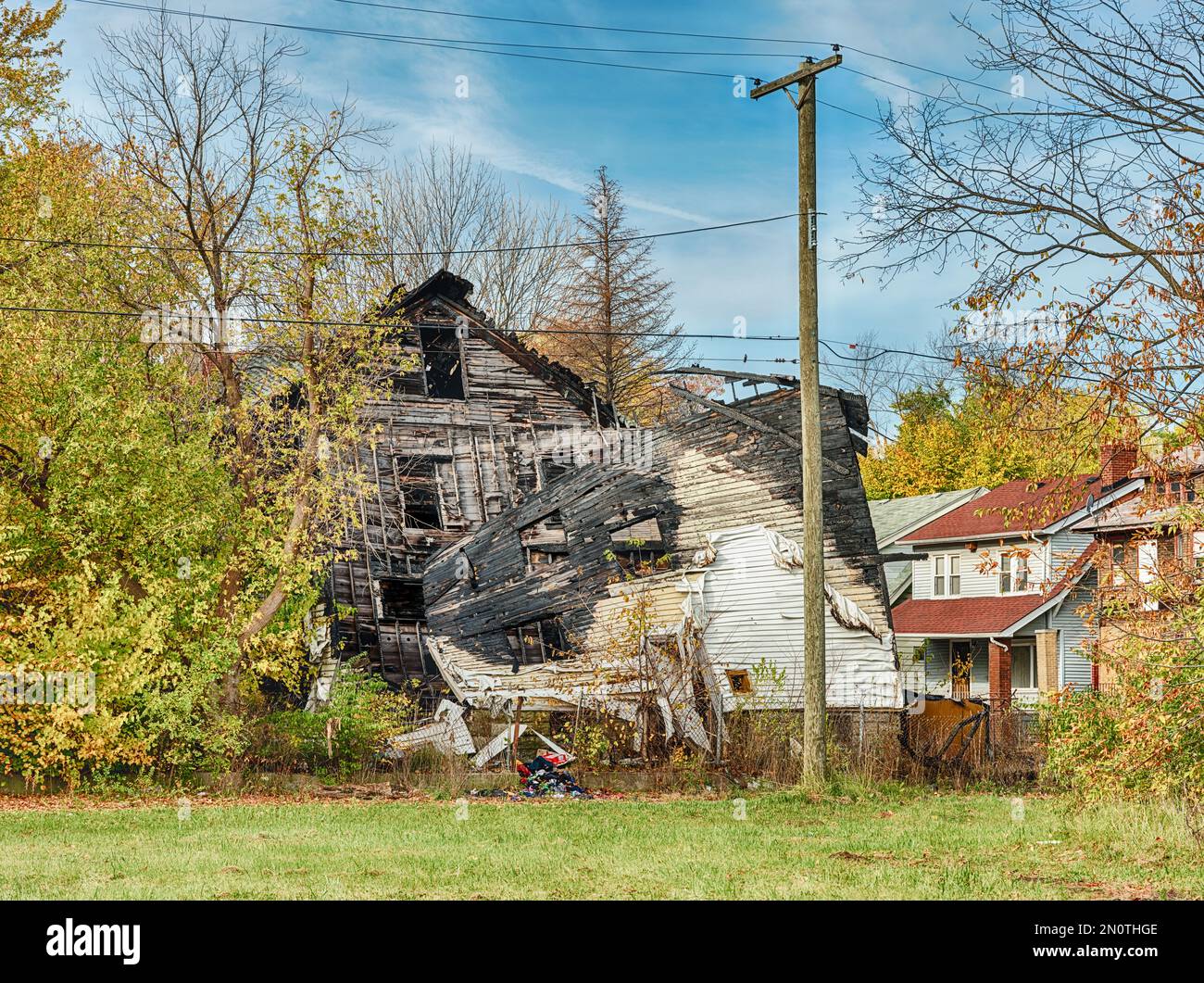 Un lotto vuoto si trova di fronte ad una casa danneggiata da incendio e cadendo con negligenza. Foto Stock