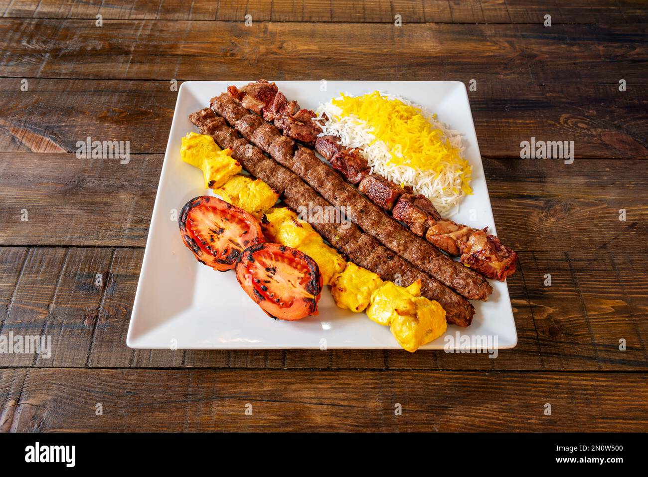 Un piatto con spiedini cucinati in stile mediorientale con diversi tipi di carne accompagnati da pomodori arrostiti e riso con salsa Foto Stock