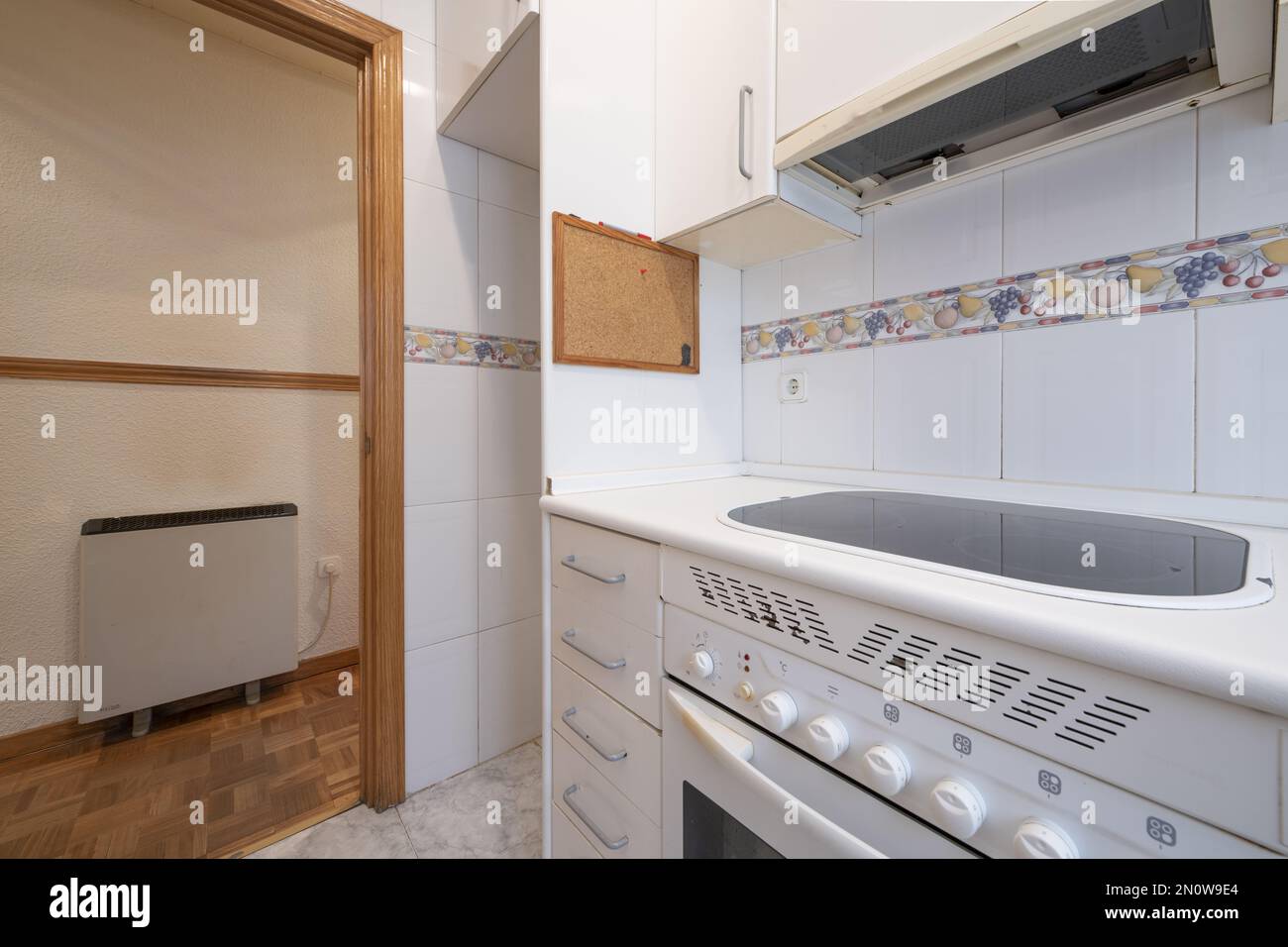 Angolo di una piccola cucina con mobili bianchi con piano cottura in vetroceramica e cappa Foto Stock