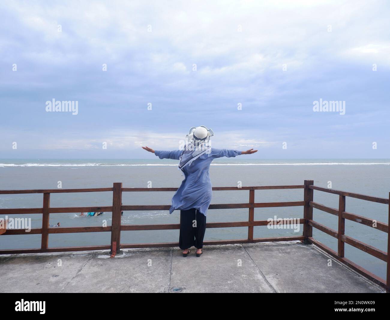 Dietro la donna nel cappello sulla spiaggia tropicale che guardava il cielo e il mare dal ponte. vista mare Foto Stock