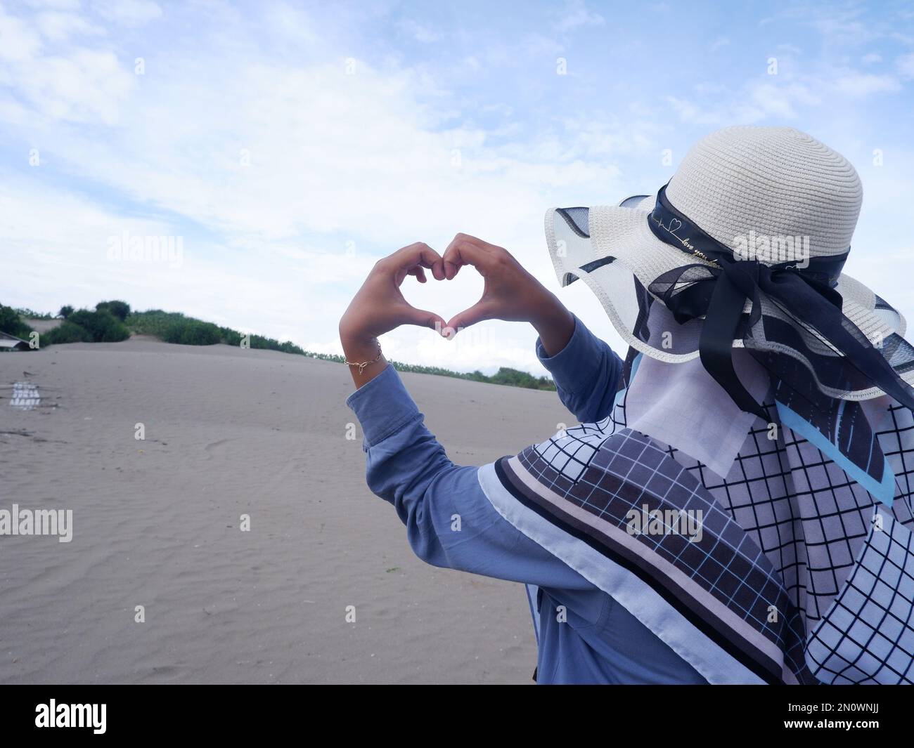 Dietro la donna nel cappello sulla spiaggia tropicale che fissava l'oceano, formò un amore dalla mano. sfondo di sabbia e cielo. essere Foto Stock