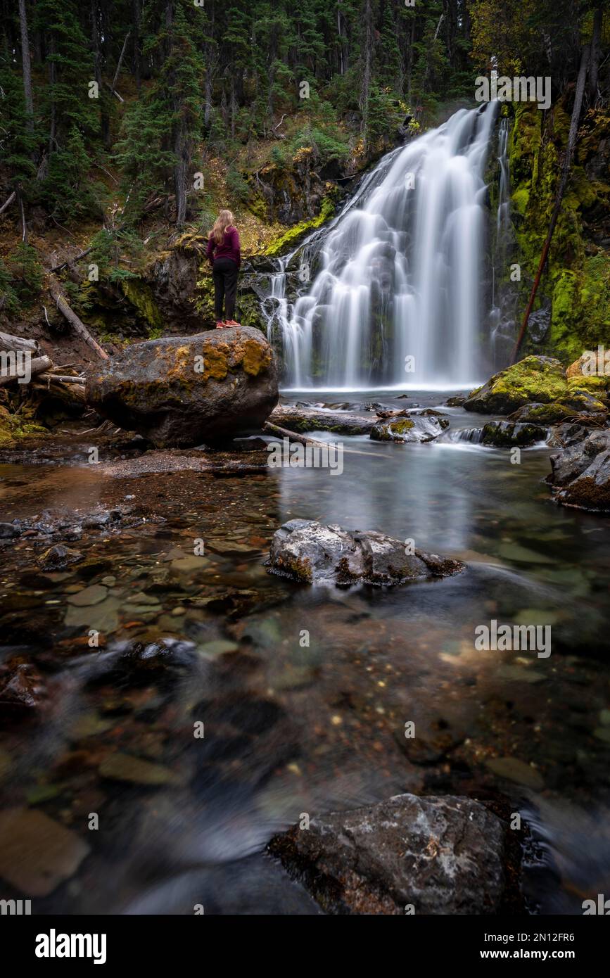 Giovane donna in piedi su pietra, cascata, Middle Tumalo Falls, lunga esposizione, Tumalo Creek, Bend, Contea di Deschutes, Oregon, Stati Uniti, Nord America Foto Stock