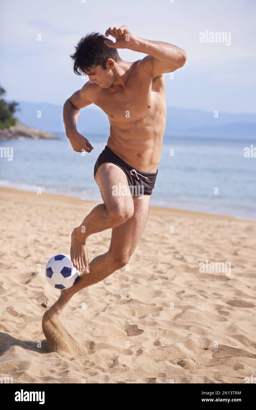 Calcio in spiaggia. Un bel giovane che gioca a calcio sulla spiaggia. Foto Stock