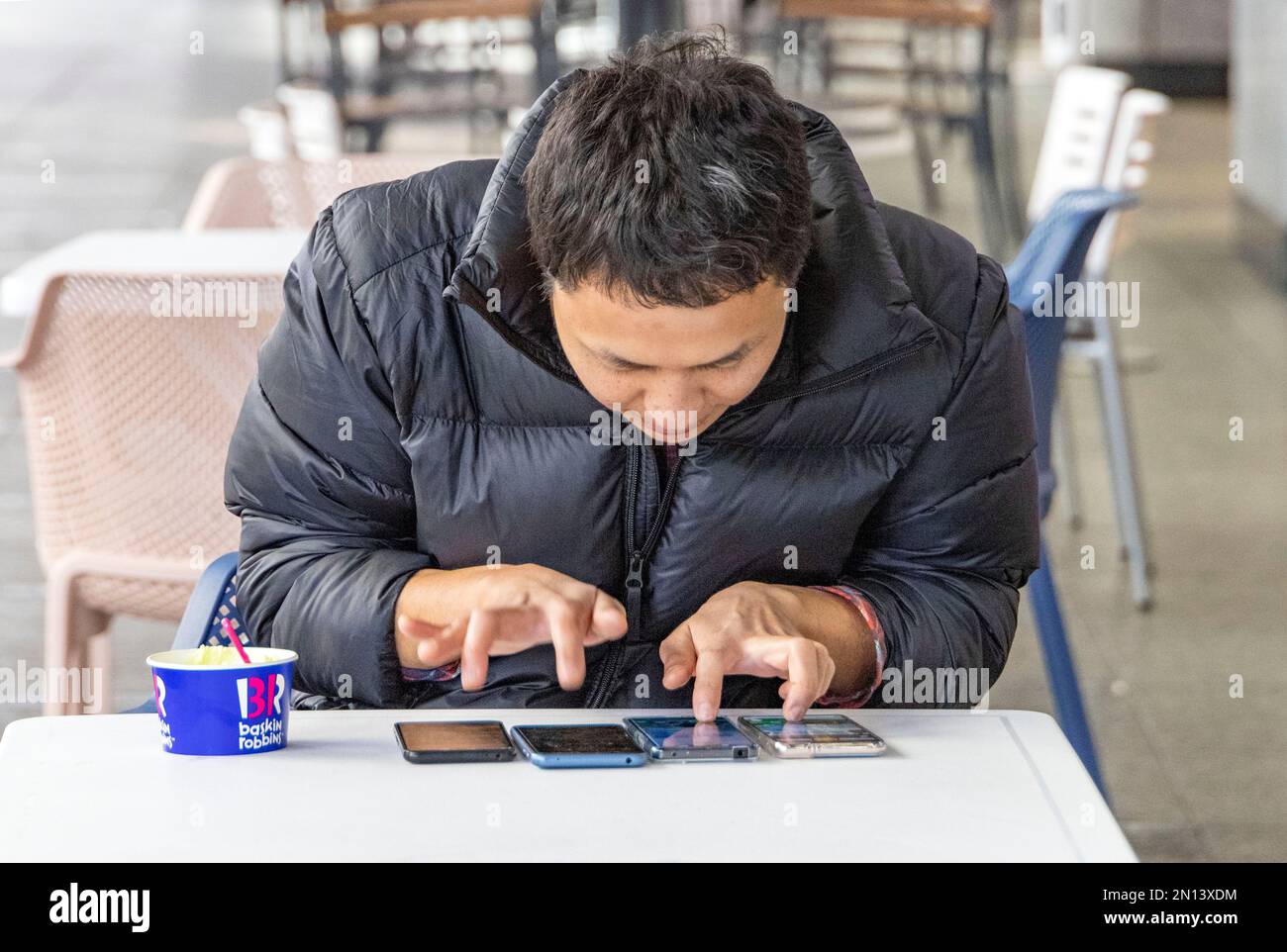 Uomo giapponese che gioca o tocca quattro telefoni alla volta possibilmente giocando una partita Foto Stock