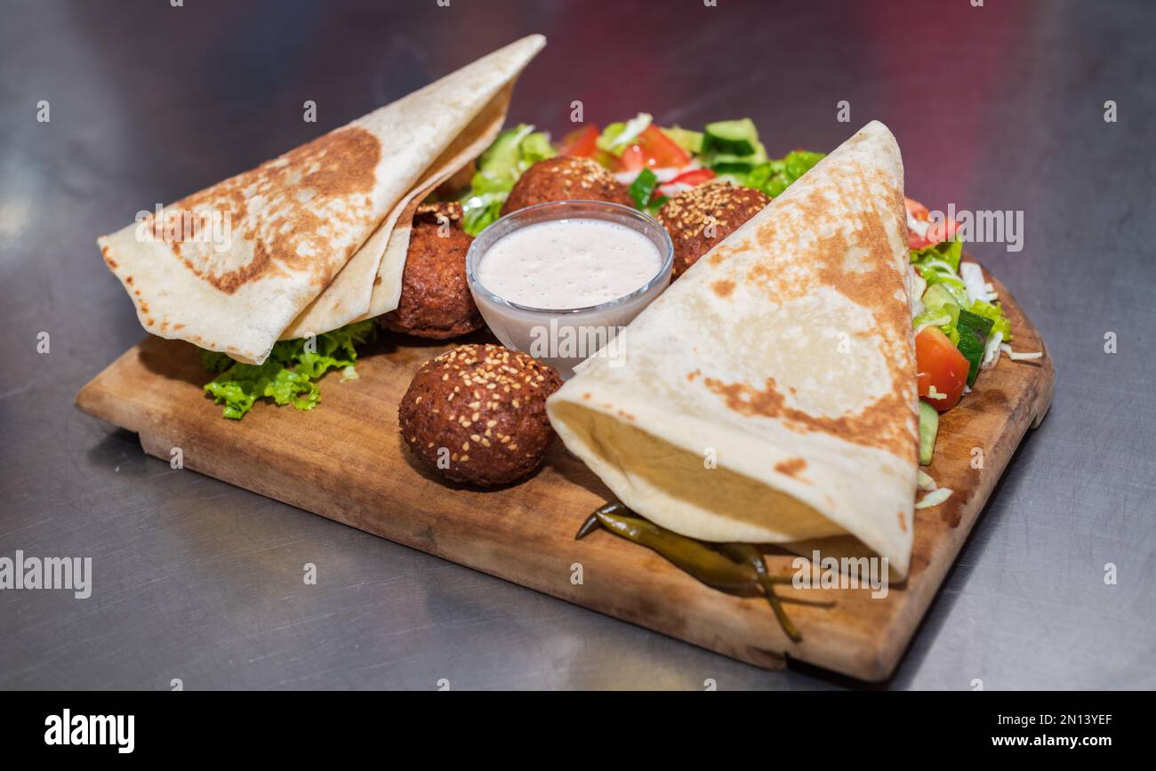 Presentazione del piatto libanese medio orientale Falafel su un piatto di legno. tortilla, insalata di verdure e salsa tahini. Foto Stock