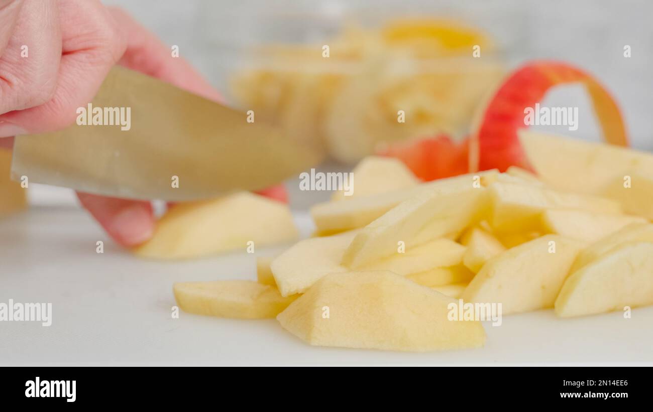 Fette di mela, e la mela buccia primo piano su un tagliere bianco sul tavolo da cucina. Donna affettare mele, ricetta torta di mele Foto Stock