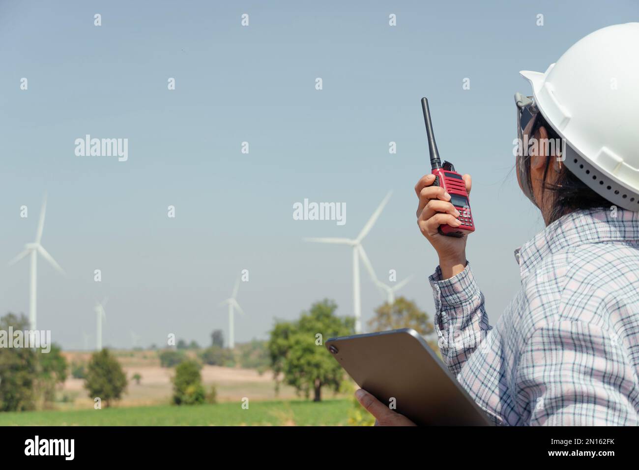 Ingegnere donna che comunica con il team di lavoro da walkie-talkie su installazione turbine eoliche per generare energia elettrica per la comunità. Foto Stock