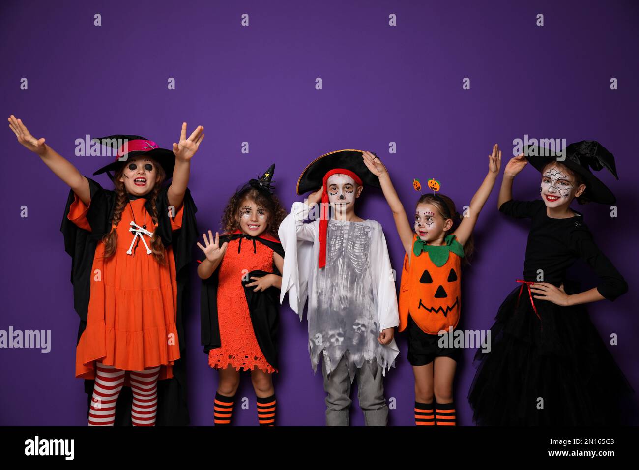 Carino bambini che indossano costumi di Halloween su sfondo viola Foto Stock