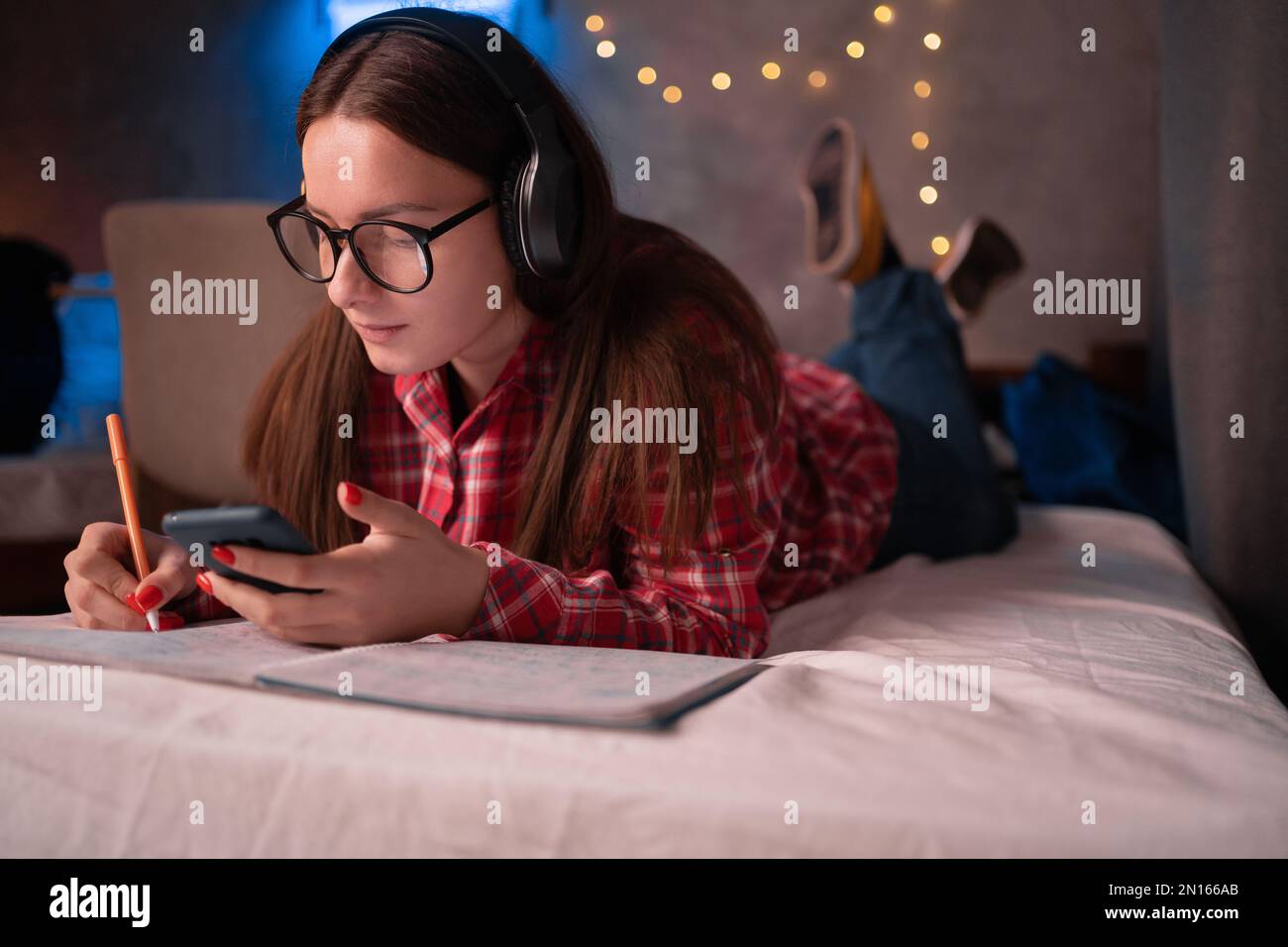 Studente ragazza adolescente con telefono cellulare per l'apprendimento a distanza utilizzando l'applicazione mobile, guardando online insegnamento studiare in dormitorio utilizzando app Foto Stock